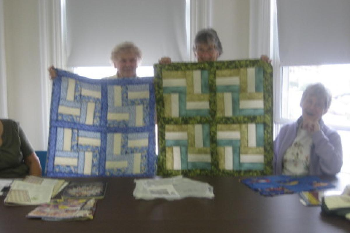 Women Holding Blue and Green Quilts